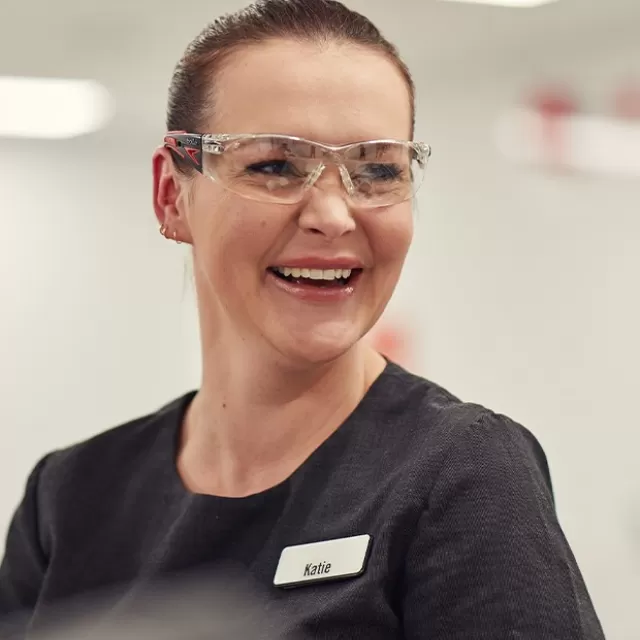 a nurse is wearing goggles and scrubs and smiling off camera