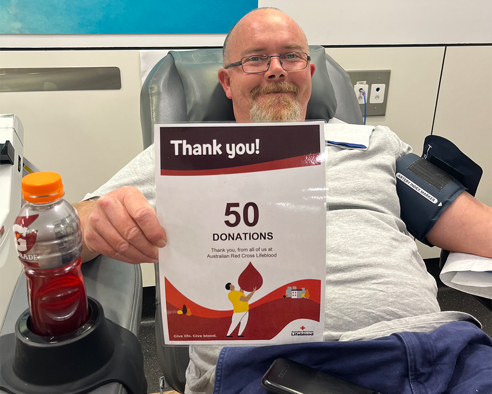 man in the donor chair holding a sign saying Thank You 50 donations