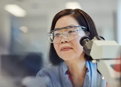 close up of a scientist wearing goggles sitting next to a microscope